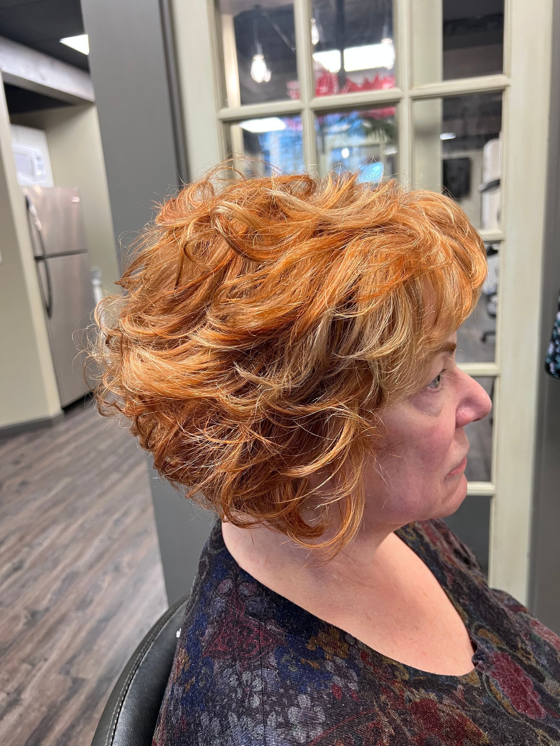 A woman with red hair is sitting in a chair in front of a window.