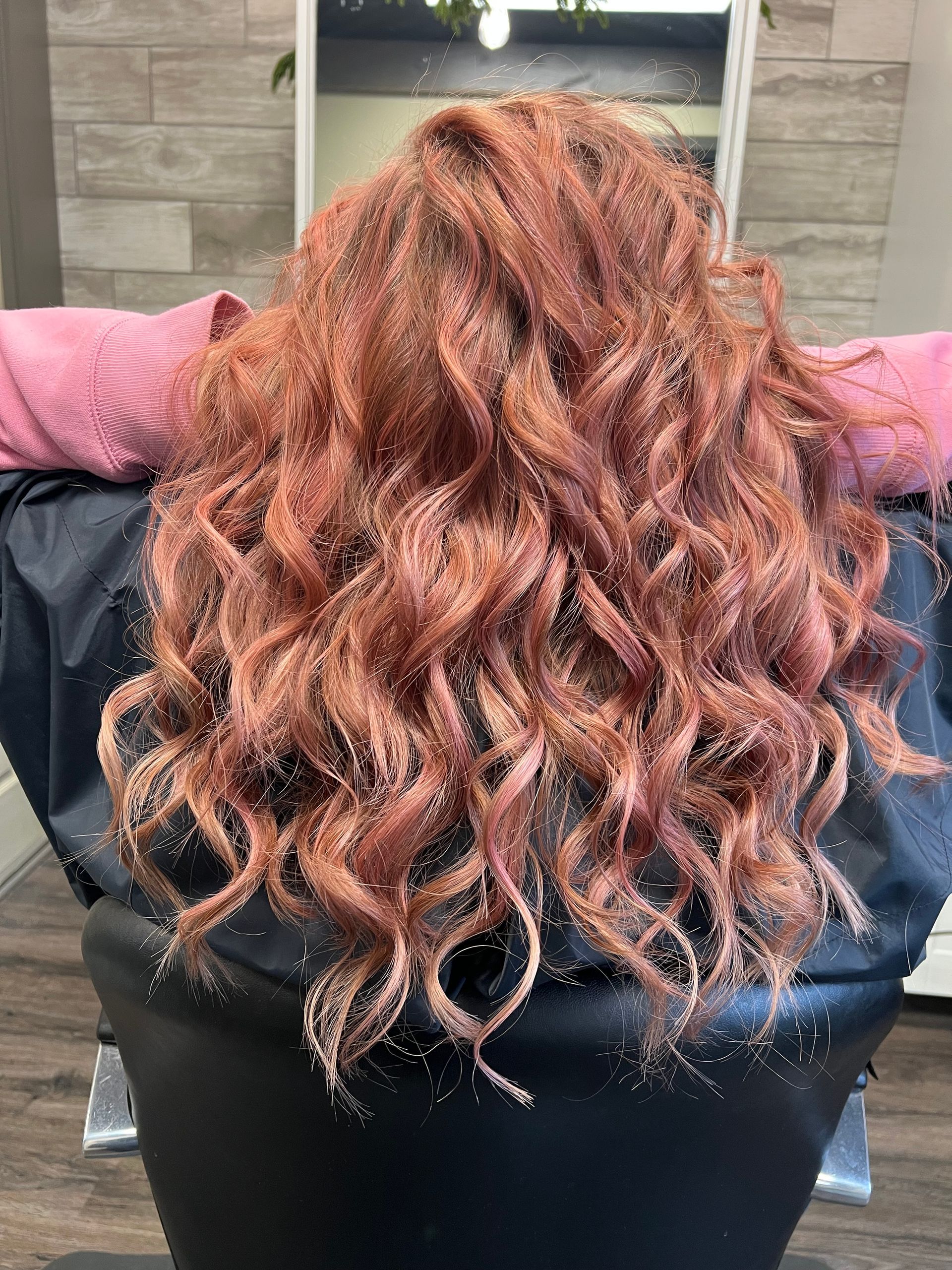 A woman with red curly hair is sitting in a chair in front of a mirror.