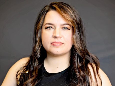 A woman with long brown hair is wearing a black tank top and looking at the camera.