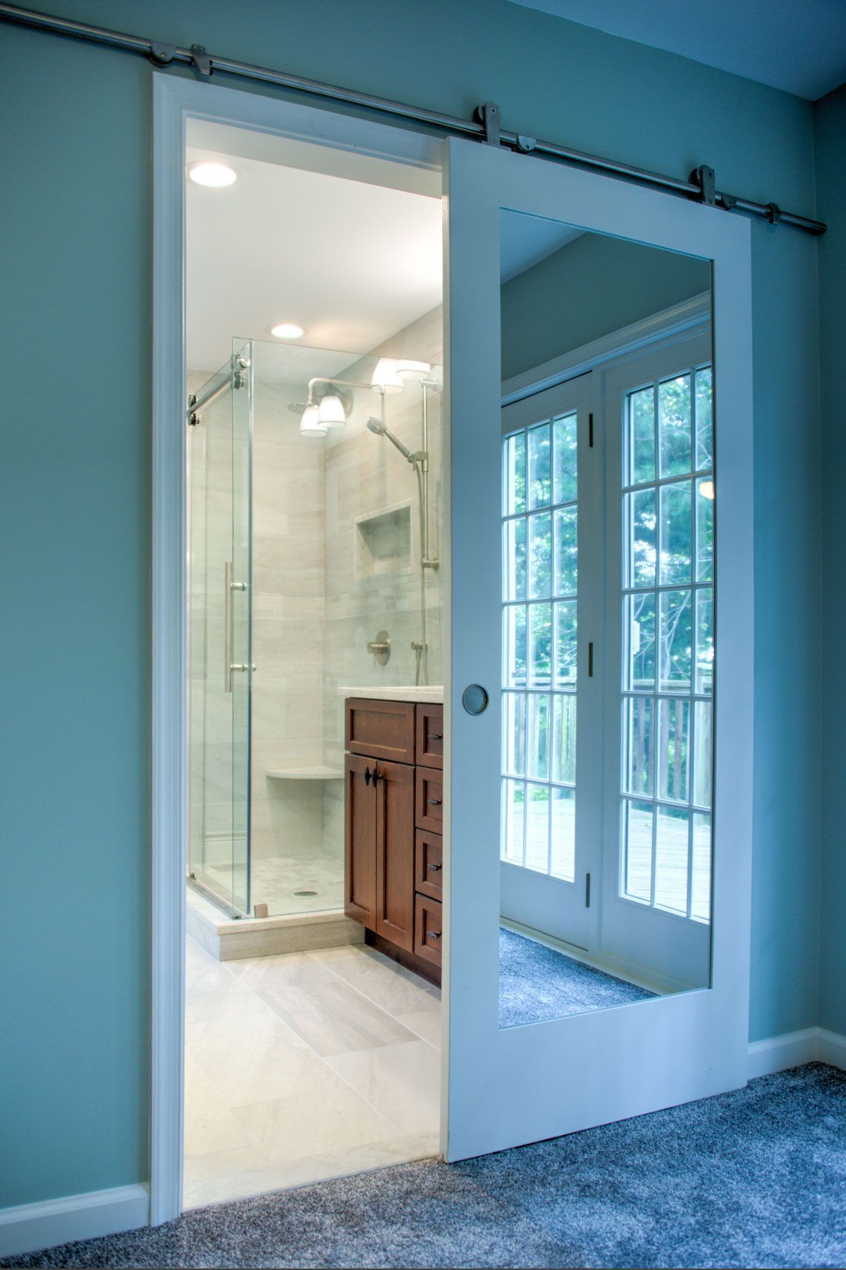 Sliding door reveals a bathroom with glass shower and vanity, also a view of French doors