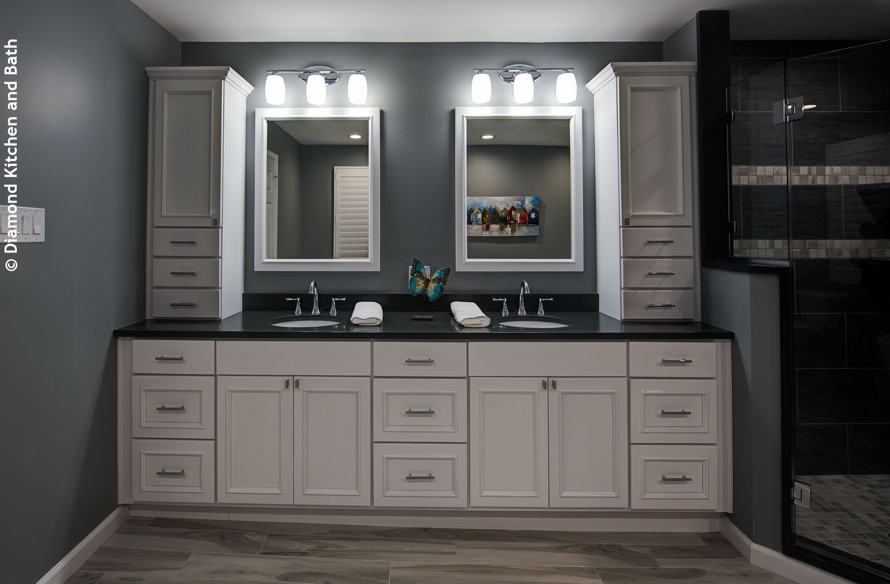 Bathroom with dual sinks, white cabinets, dark countertop, gray walls, and tall storage cabinets