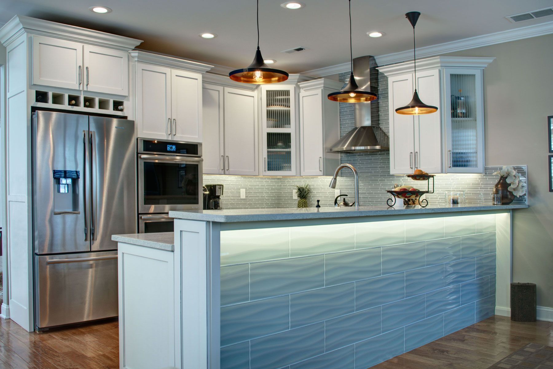 Modern kitchen with white cabinets, stainless steel appliances, blue tiled island, and pendant lights