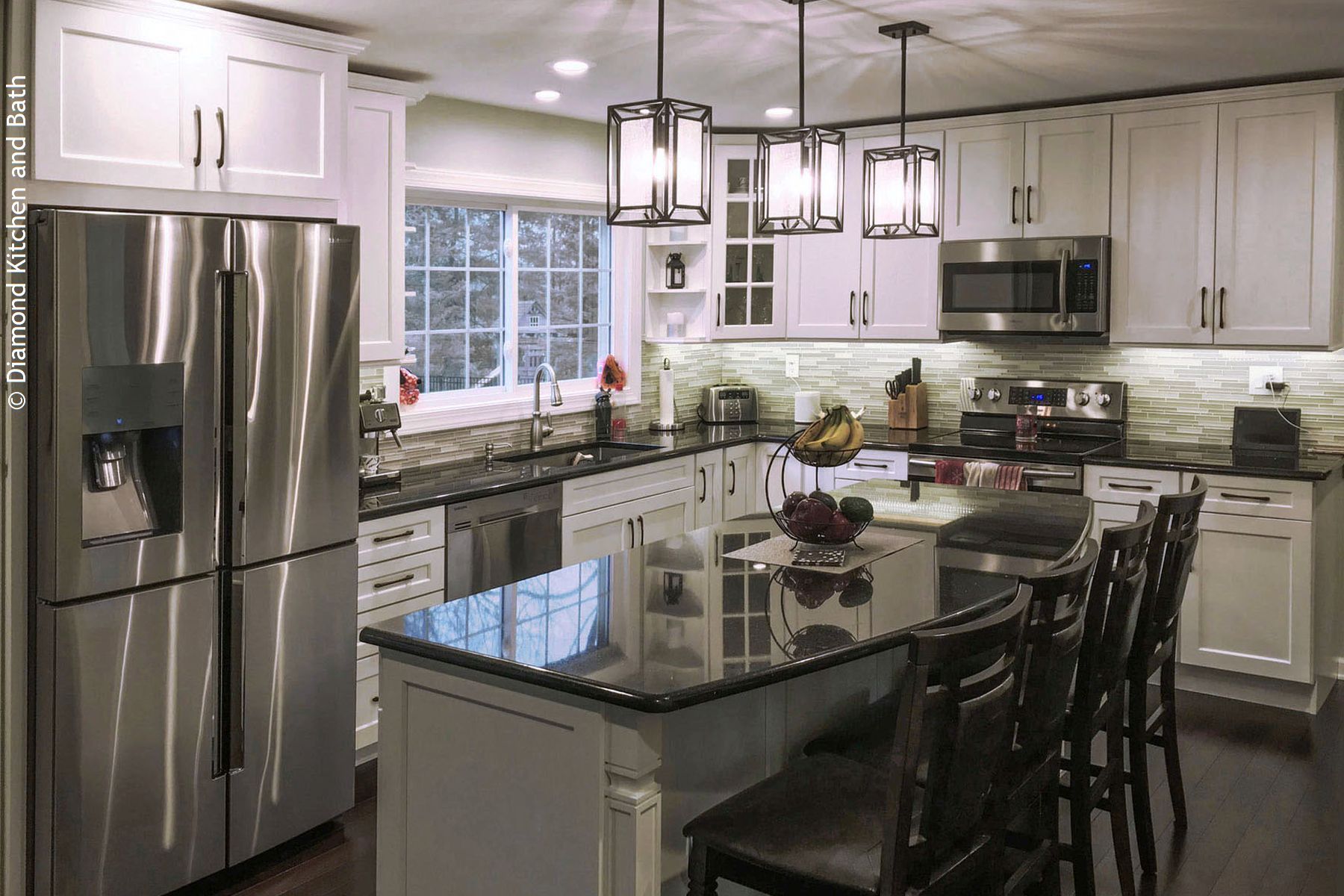 Modern white kitchen with stainless steel appliances, dark countertops, and island with bar stools