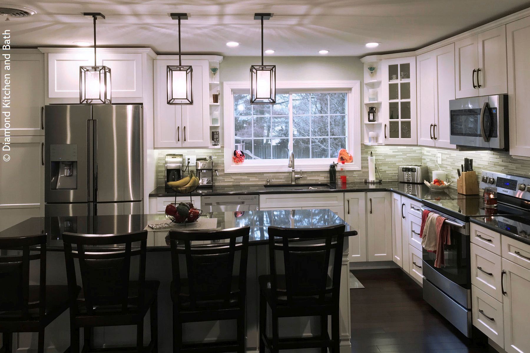 Modern white kitchen with black island, stainless steel appliances, and pendant lights