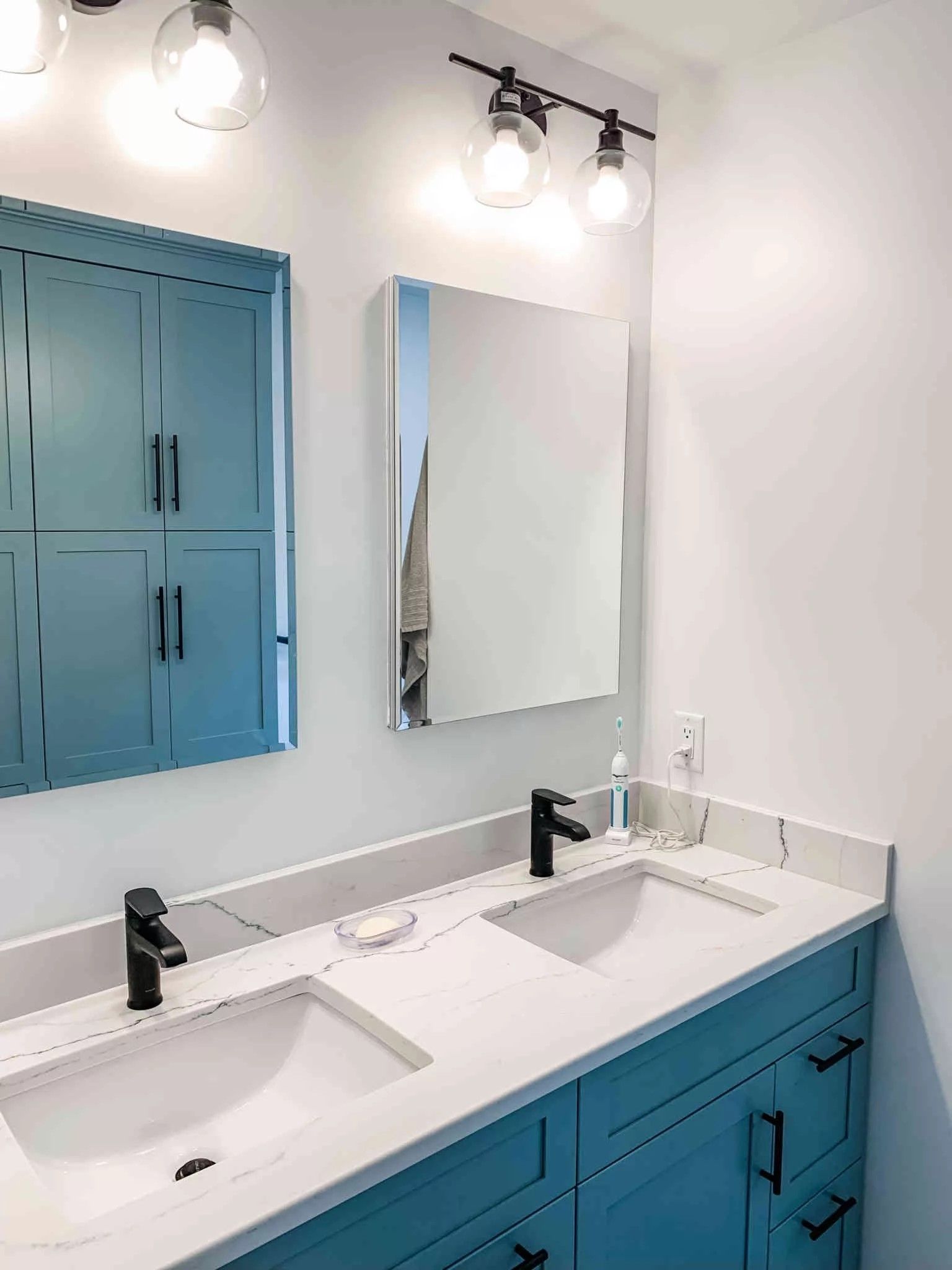 Blue vanity with two sinks, two mirrors, and overhead lighting in a modern bathroom