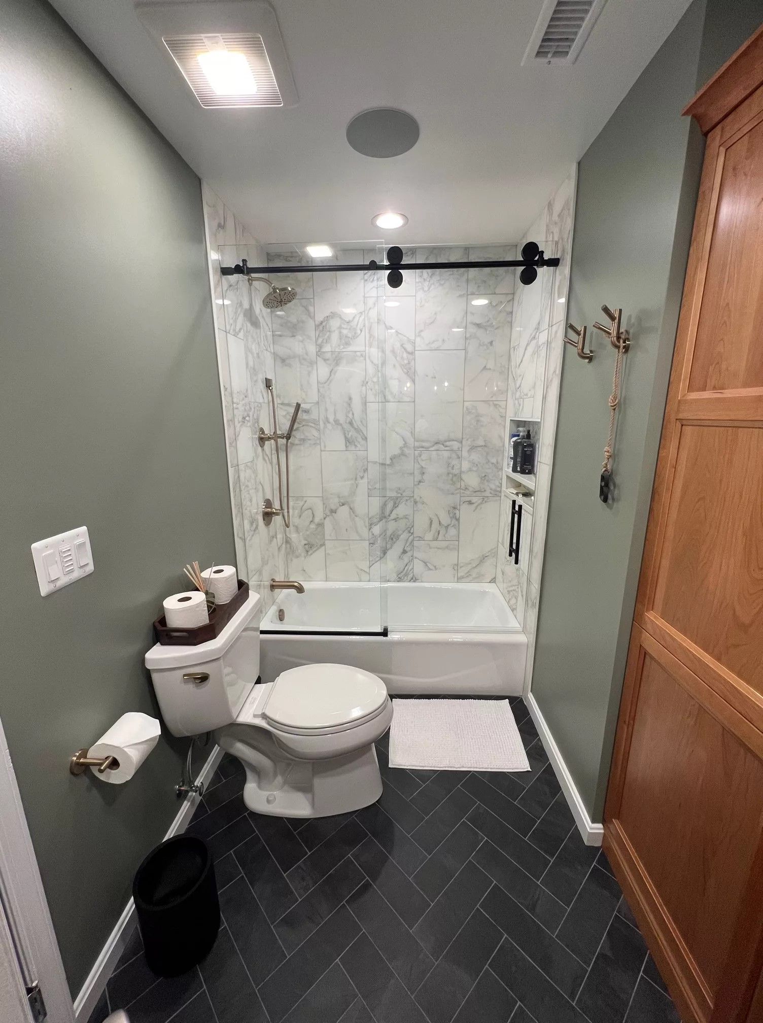 Bathroom with marble shower, herringbone floor, sage walls, and wooden cabinet