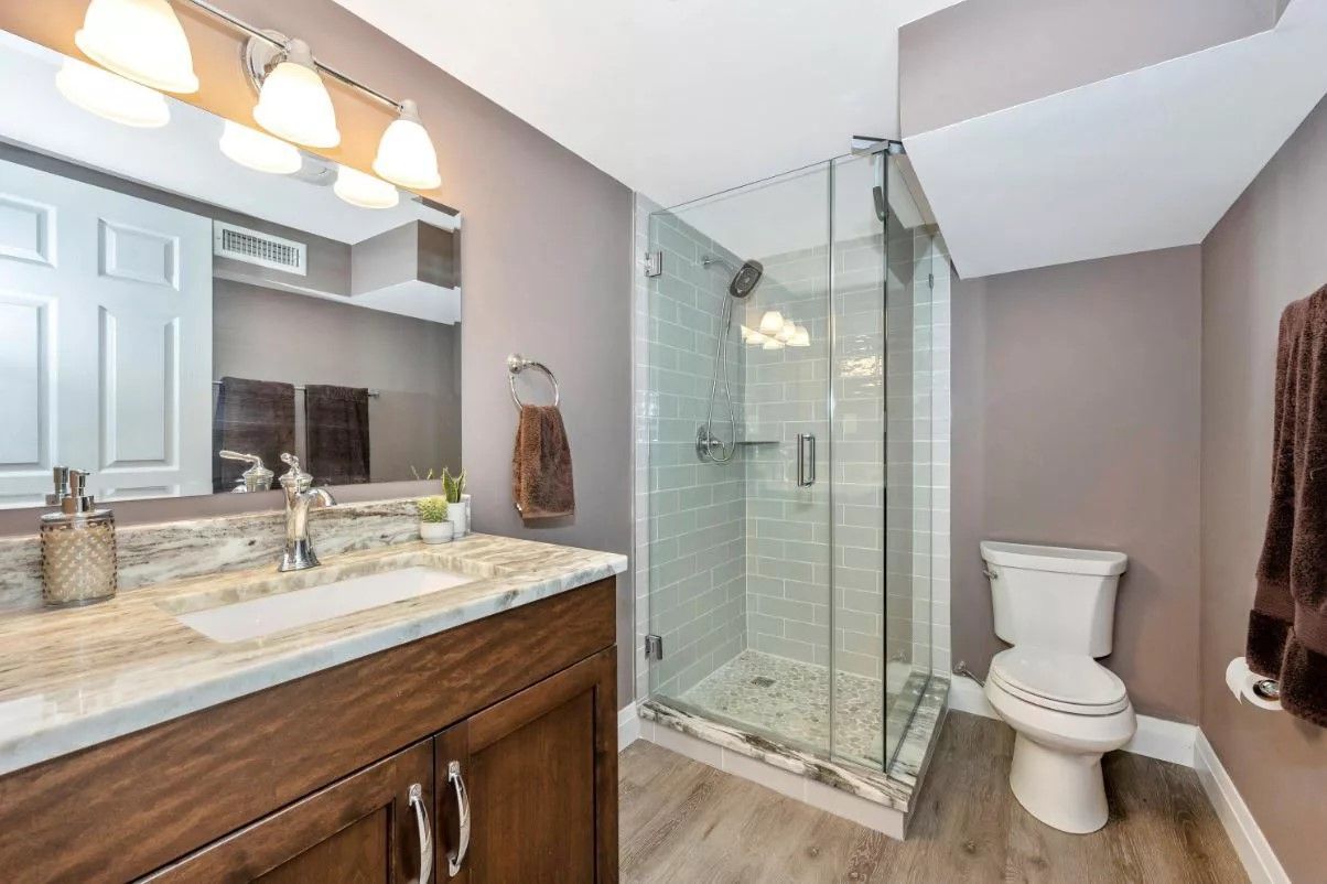 Bathroom with a glass shower, vanity, and toilet; gray and brown color scheme