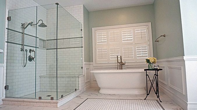 Elegant bathroom with glass shower, white tub, and shuttered window