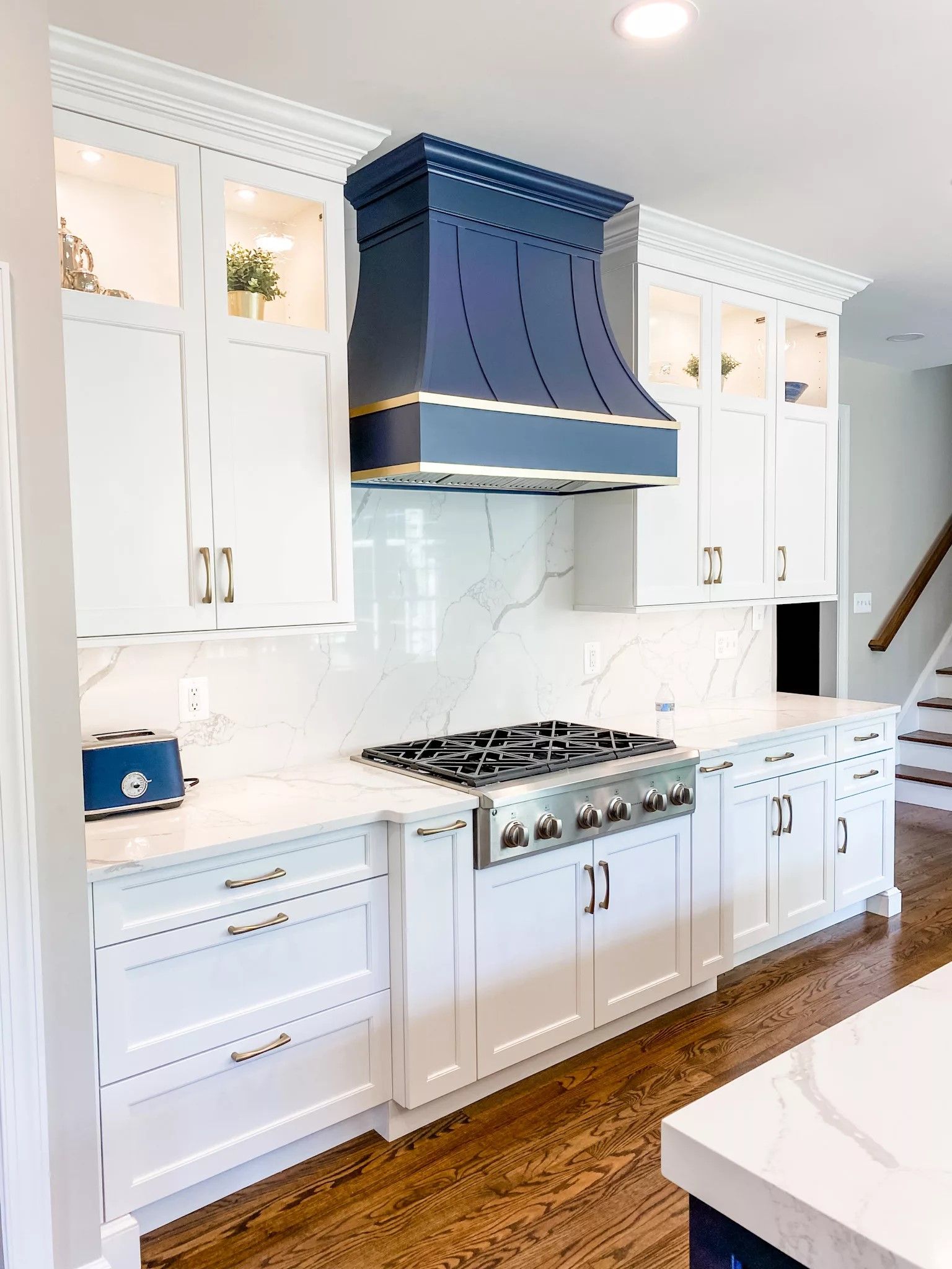 White kitchen with blue range hood, white cabinets, marble backsplash, and a gas range