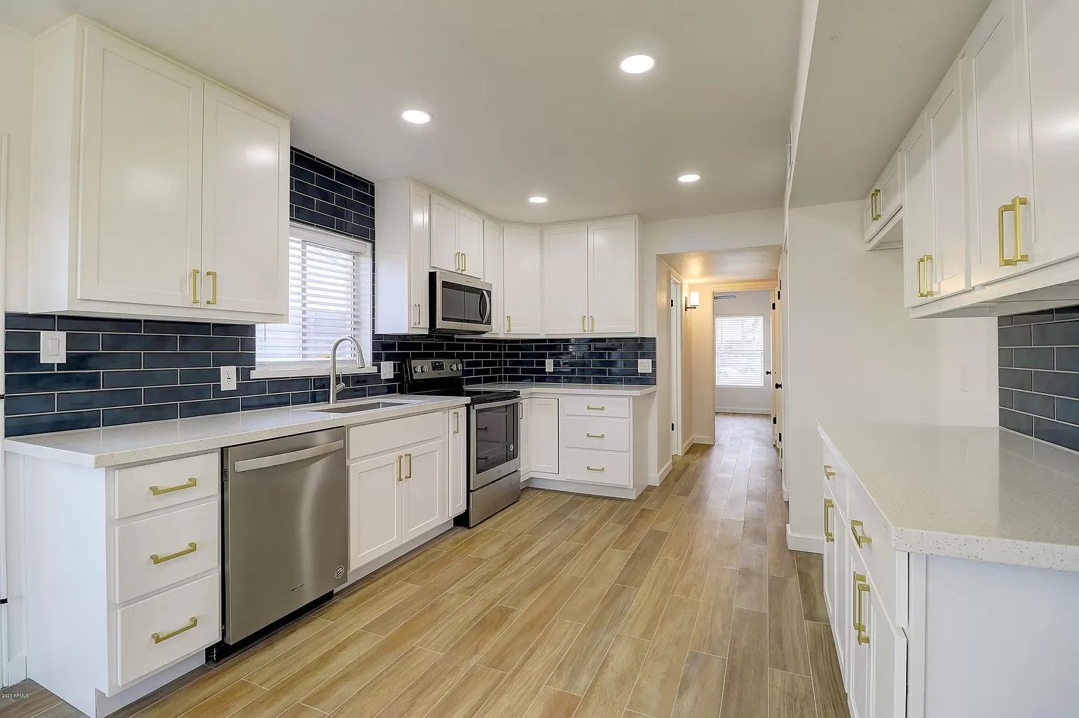 Bright white kitchen with stainless steel appliances, dark blue backsplash, and light wood flooring