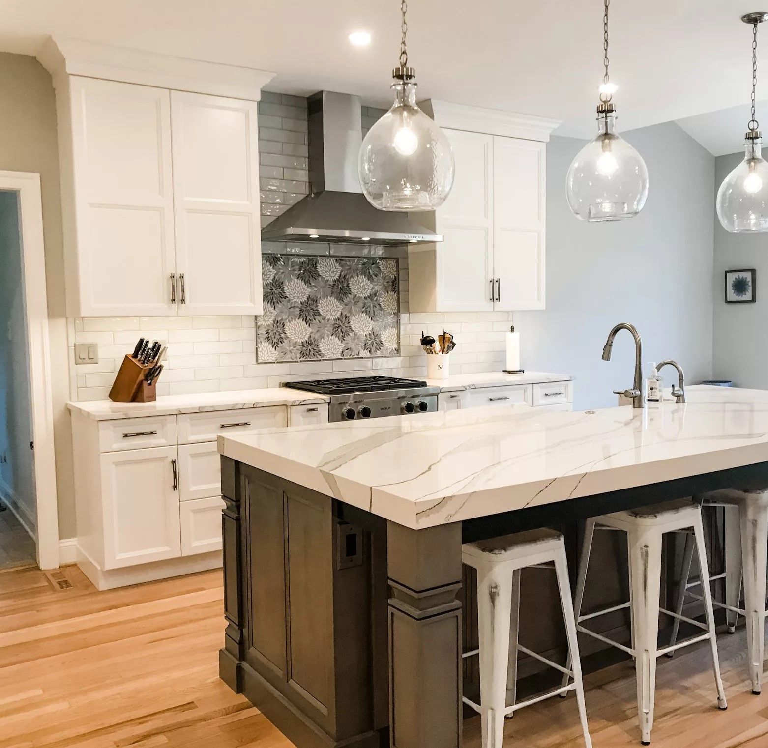 Modern kitchen with white cabinets, marble island, pendant lights, and stainless steel appliances
