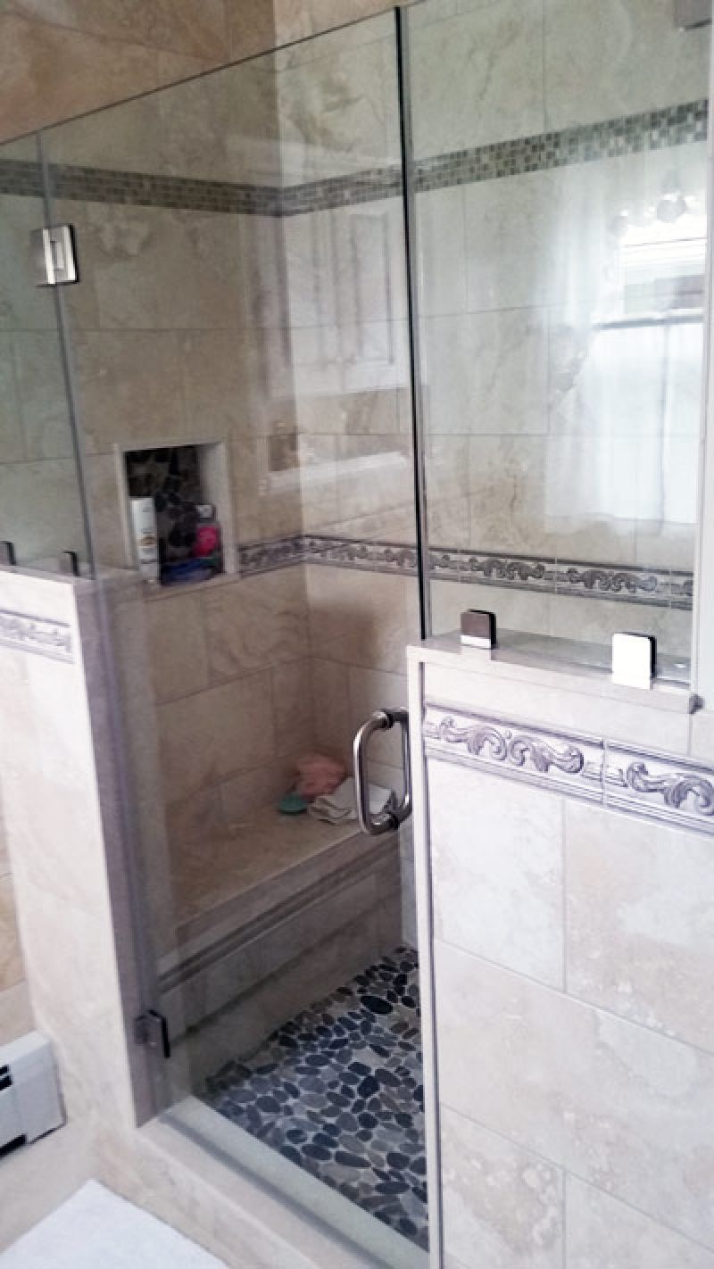 Shower stall with glass door, beige tile, stone floor, built-in bench, and a niche for toiletries