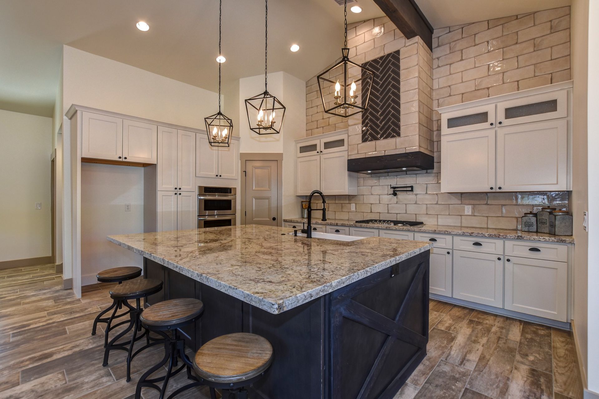 Modern kitchen with dark island and granite countertop, white cabinets, brick backsplash, and pendant lights
