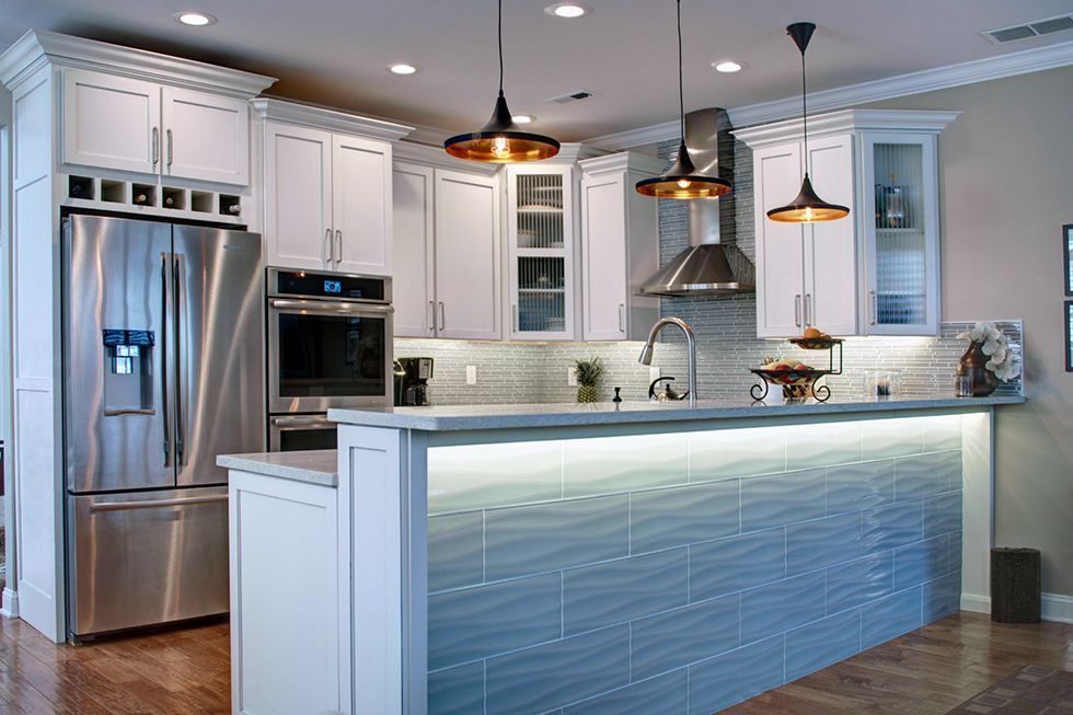 Modern kitchen with white cabinets, stainless steel appliances, and blue tiled island with pendant lights