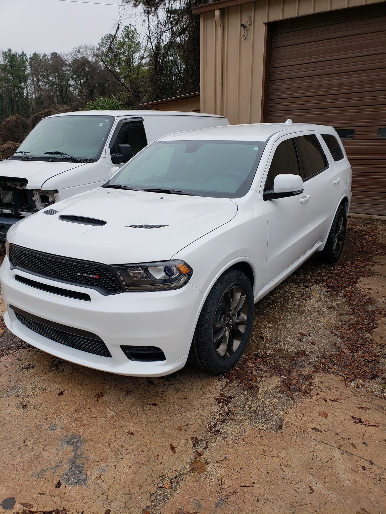 White Dodge Durango SUV parked in front of a building with a white van.