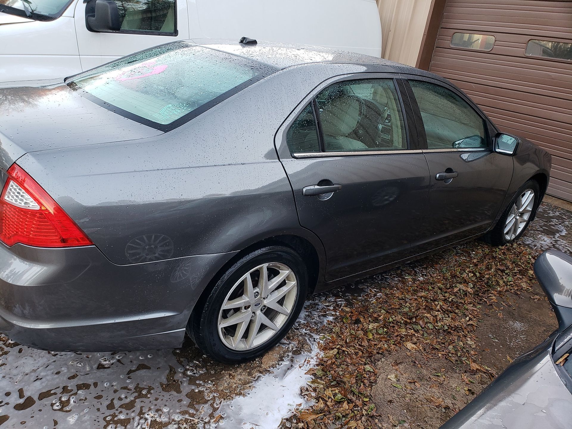 Gray sedan parked near a building with water droplets on the car.