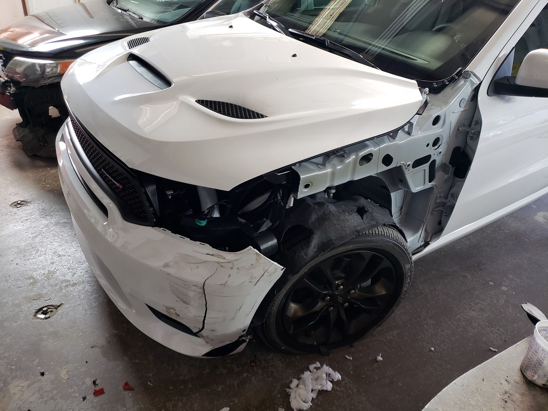 White Dodge Durango SUV with front-end damage; headlight and bumper detached. Black wheel is visible.