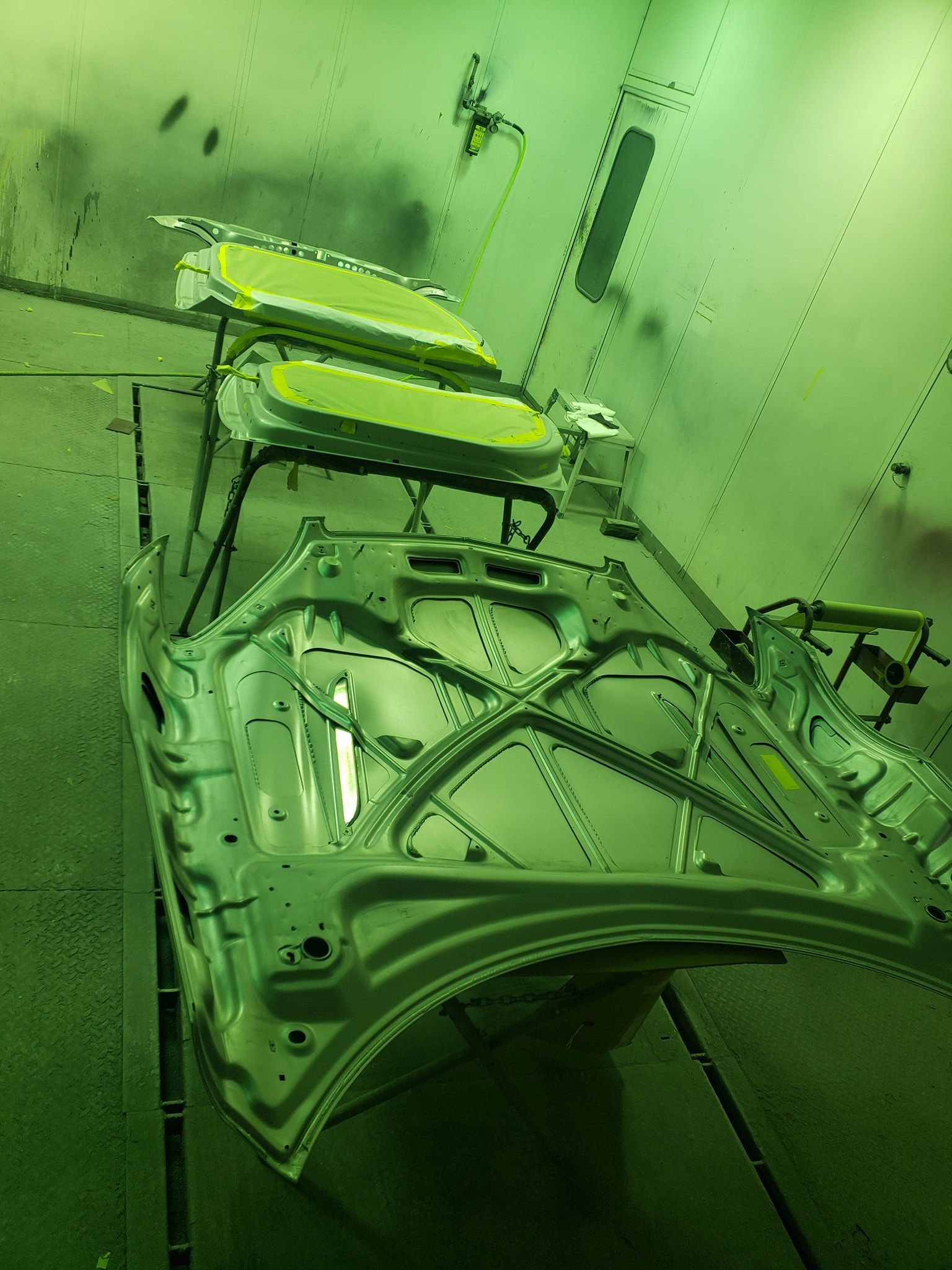 Car frame in a spray painting booth, lit with green light.