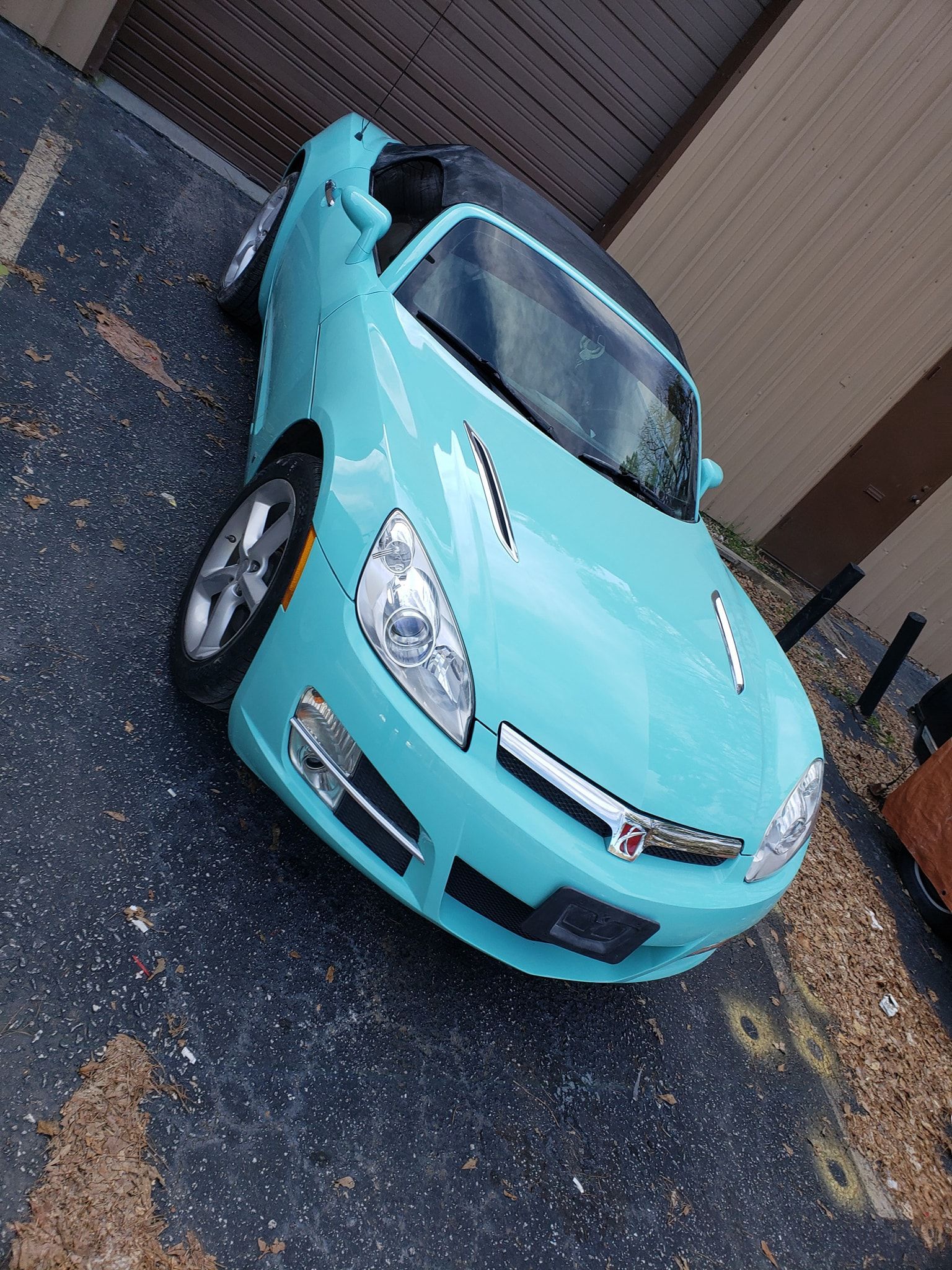 Aqua convertible car parked on a surface with debris.