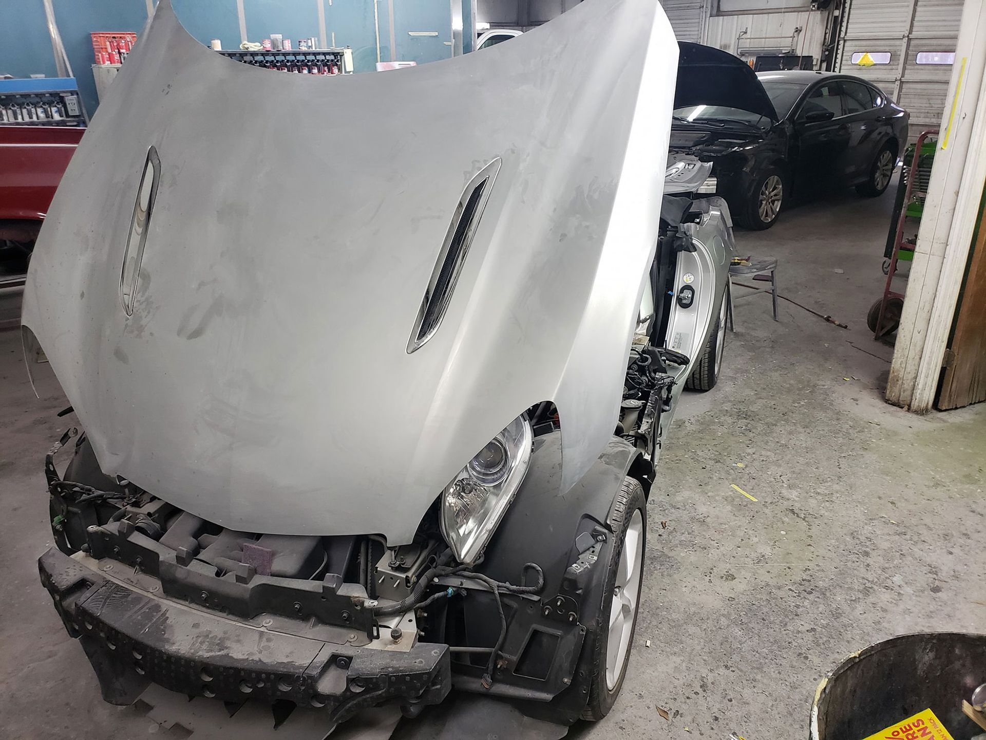 Car in auto body shop with hood open, primed for painting.