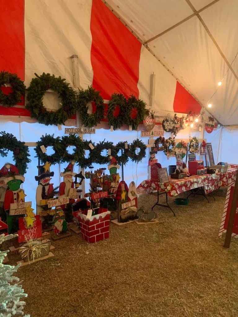 Christmas market display inside a red and white striped tent, with wreaths, wooden decorations, and a table with gifts.