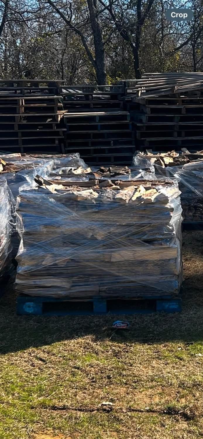 A pallet of wrapped material in a grassy area with pallets stacked in the background.