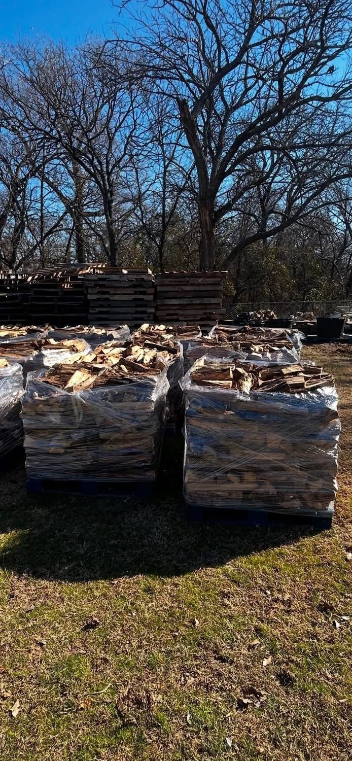 Pallets of stacked stones in a grassy area with trees and a blue sky in the background.