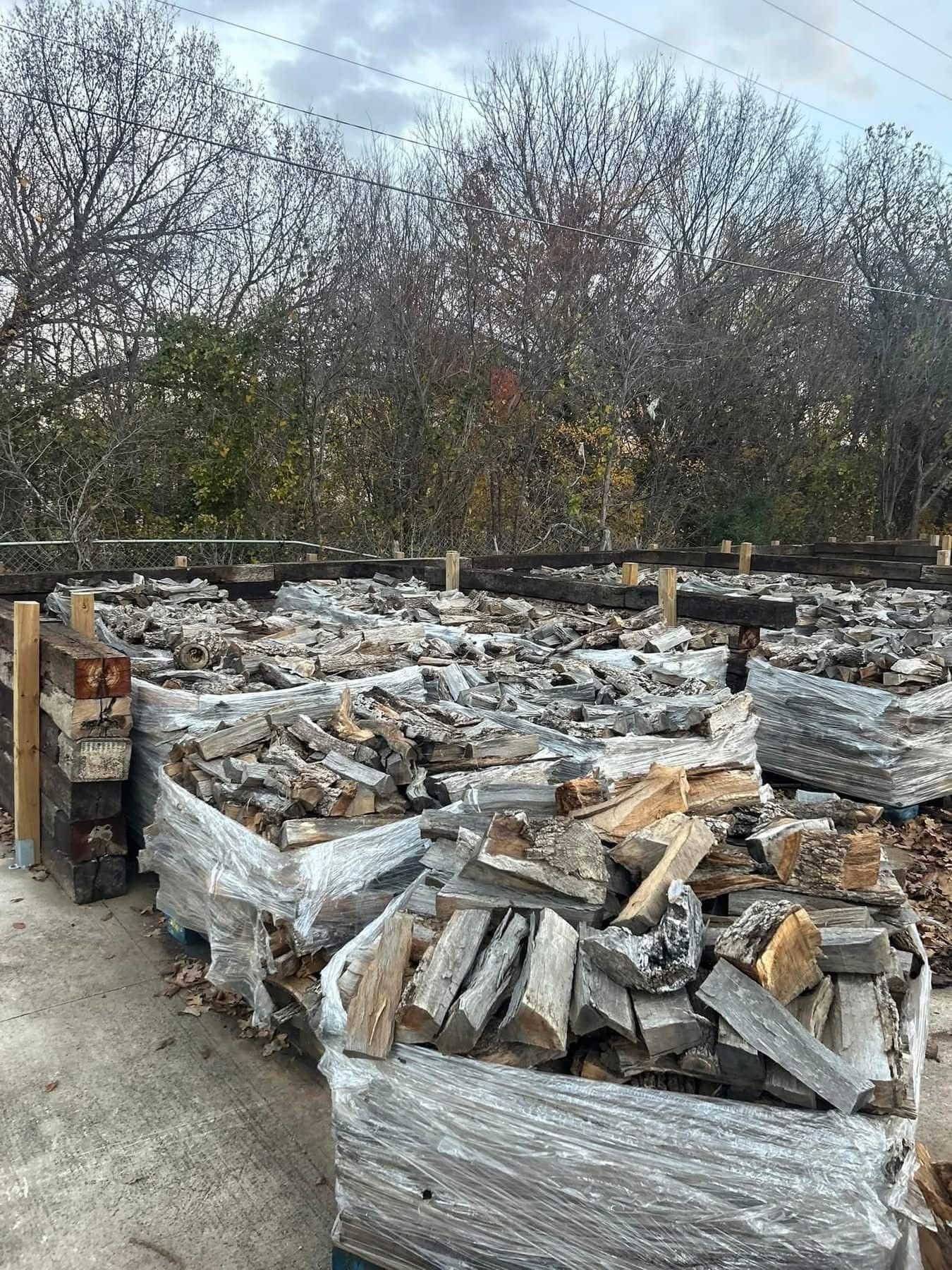 Stacks of stone and wood bundles wrapped in plastic, outdoors with trees in the background.