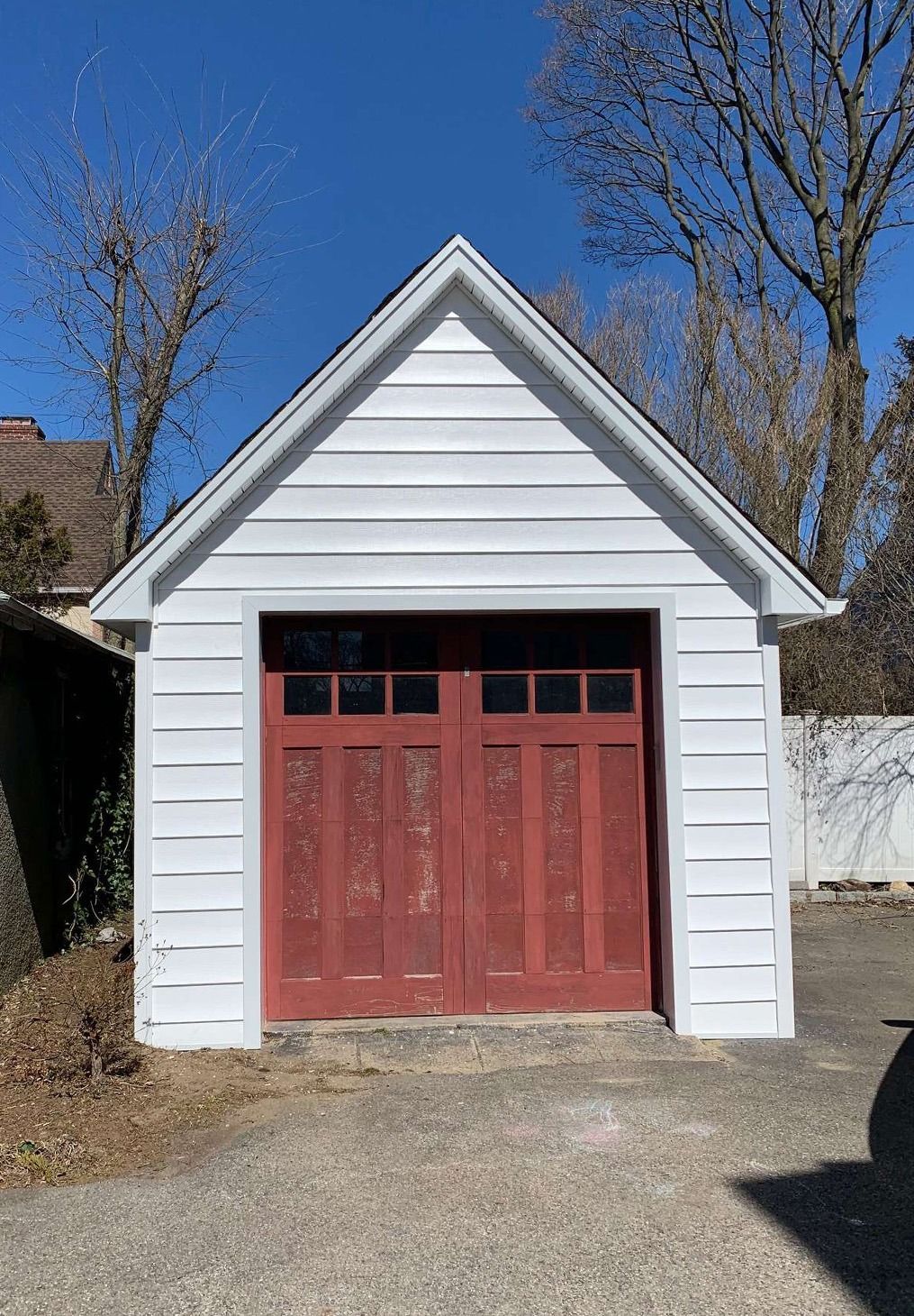 A detached white garage with a gabled roof and red wooden double doors under a clear blue sky.