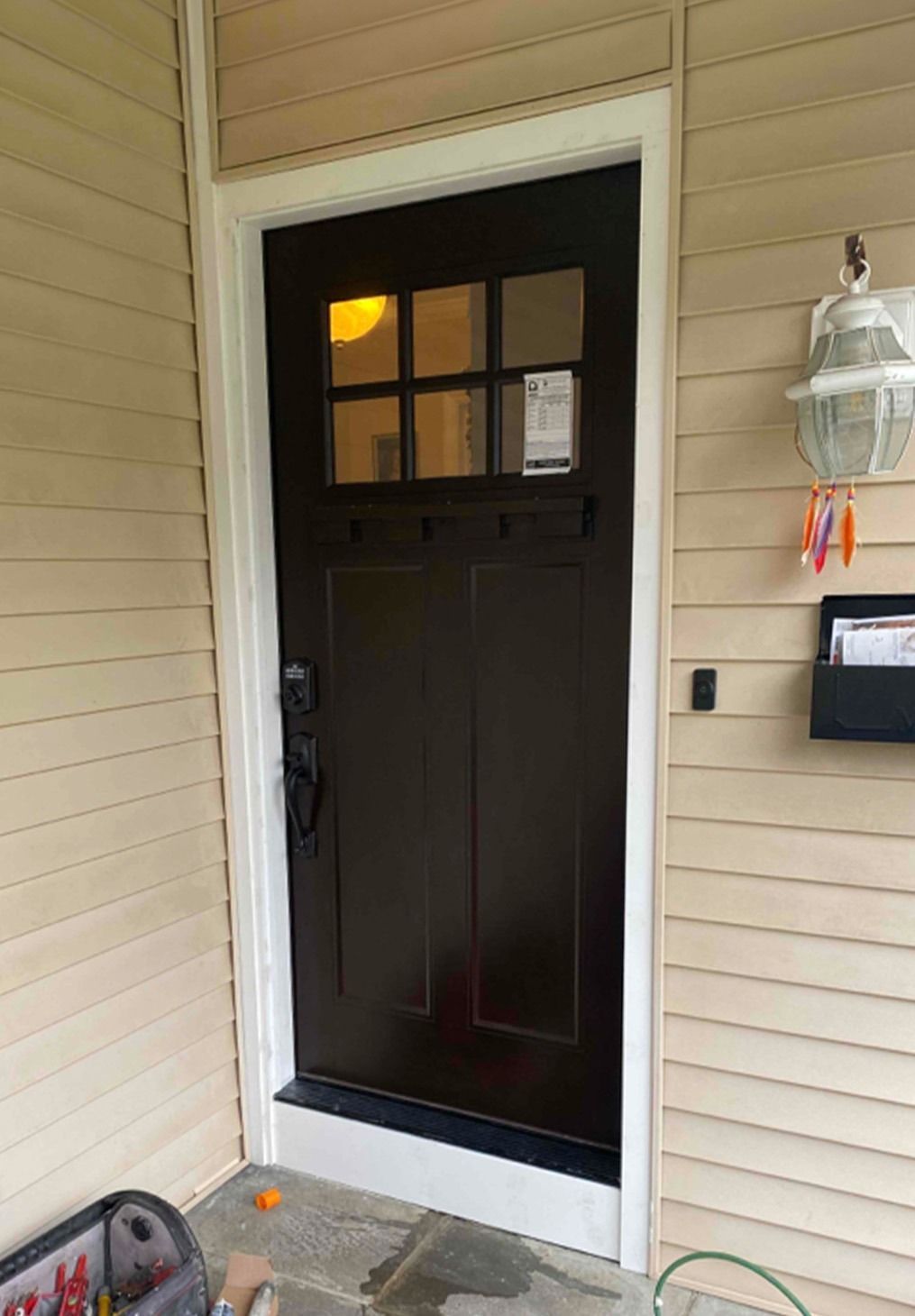 A dark brown front door with a six-pane glass window at the top, set in a house with light beige horizontal siding.