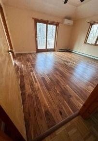 An empty room with polished hardwood floors, light walls, a glass sliding door to a balcony, and a window.