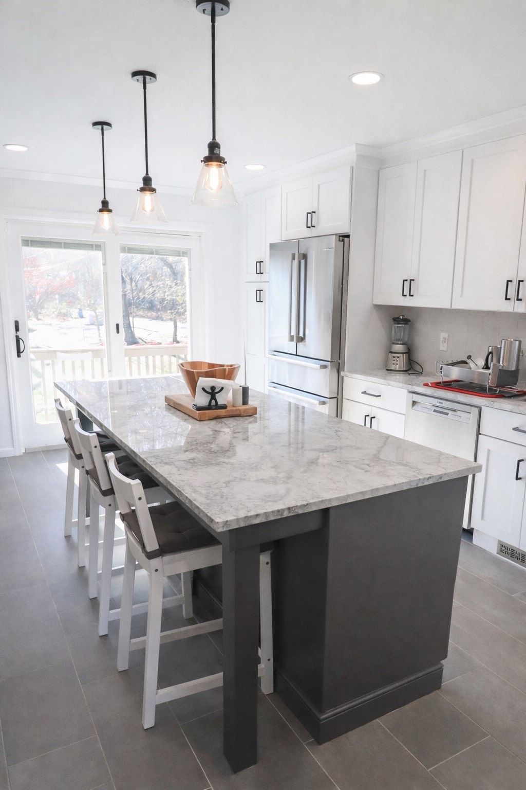 A modern kitchen with a large dark gray island, white cabinets, stainless steel appliances, and three pendant lights.