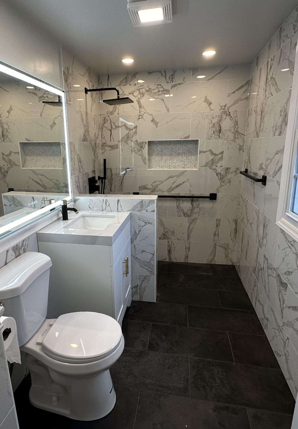 A modern bathroom featuring a white toilet, marble-tiled walk-in shower with a black grab bar, and a marble vanity.