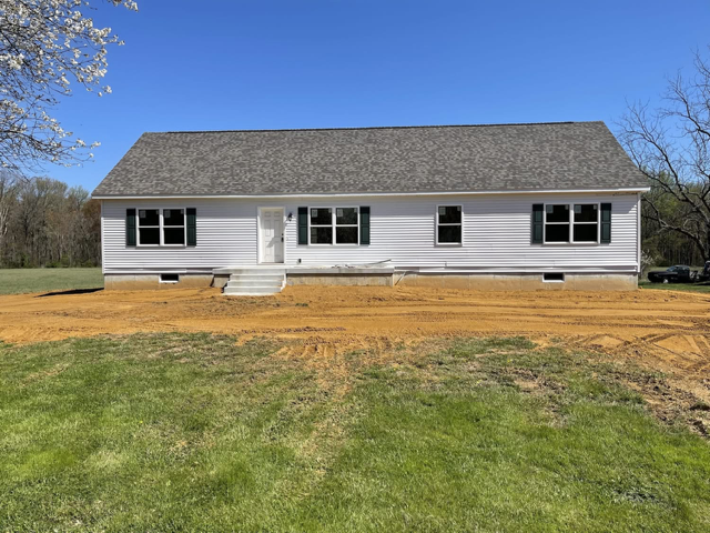 A white house with a gray roof is sitting in the middle of a grassy field