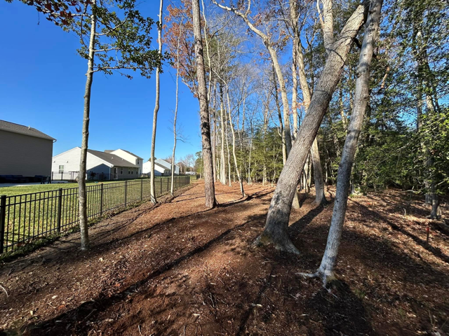A fence surrounds a lush green forest with a house in the background.