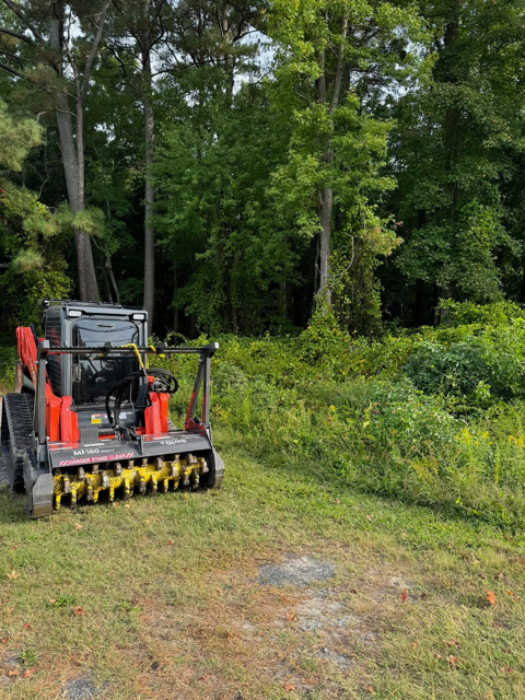 A tractor is cutting grass in a field with trees in the background.