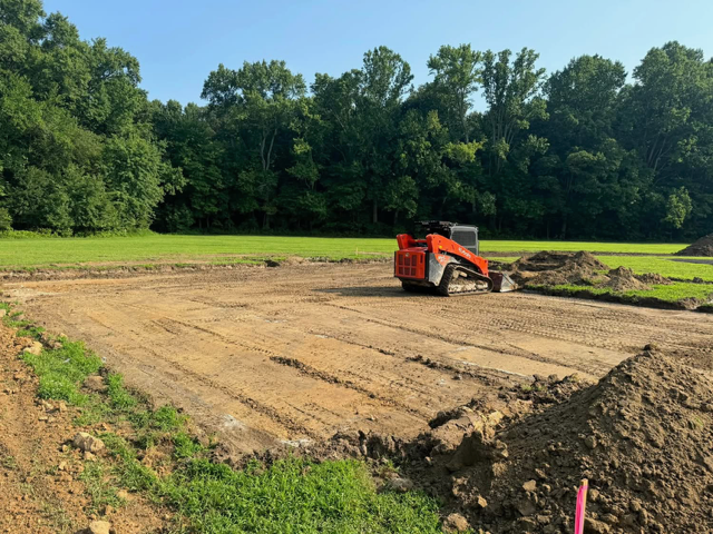 A bulldozer is moving dirt in a field with trees in the background