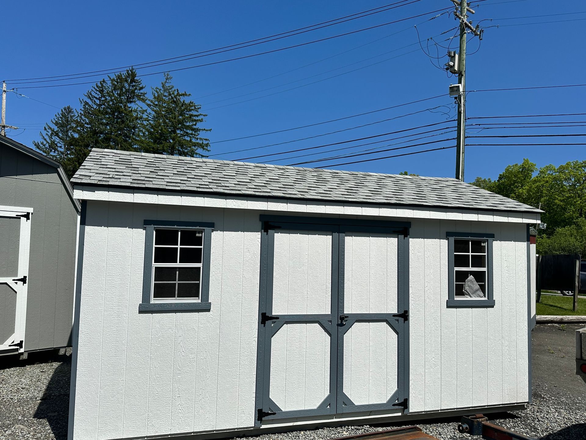 A small white shed with a gray roof and two windows.