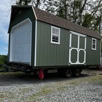 A gray barn shed is sitting on top of a dirt field.
