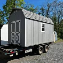 A green shed with a garage door is on a trailer.