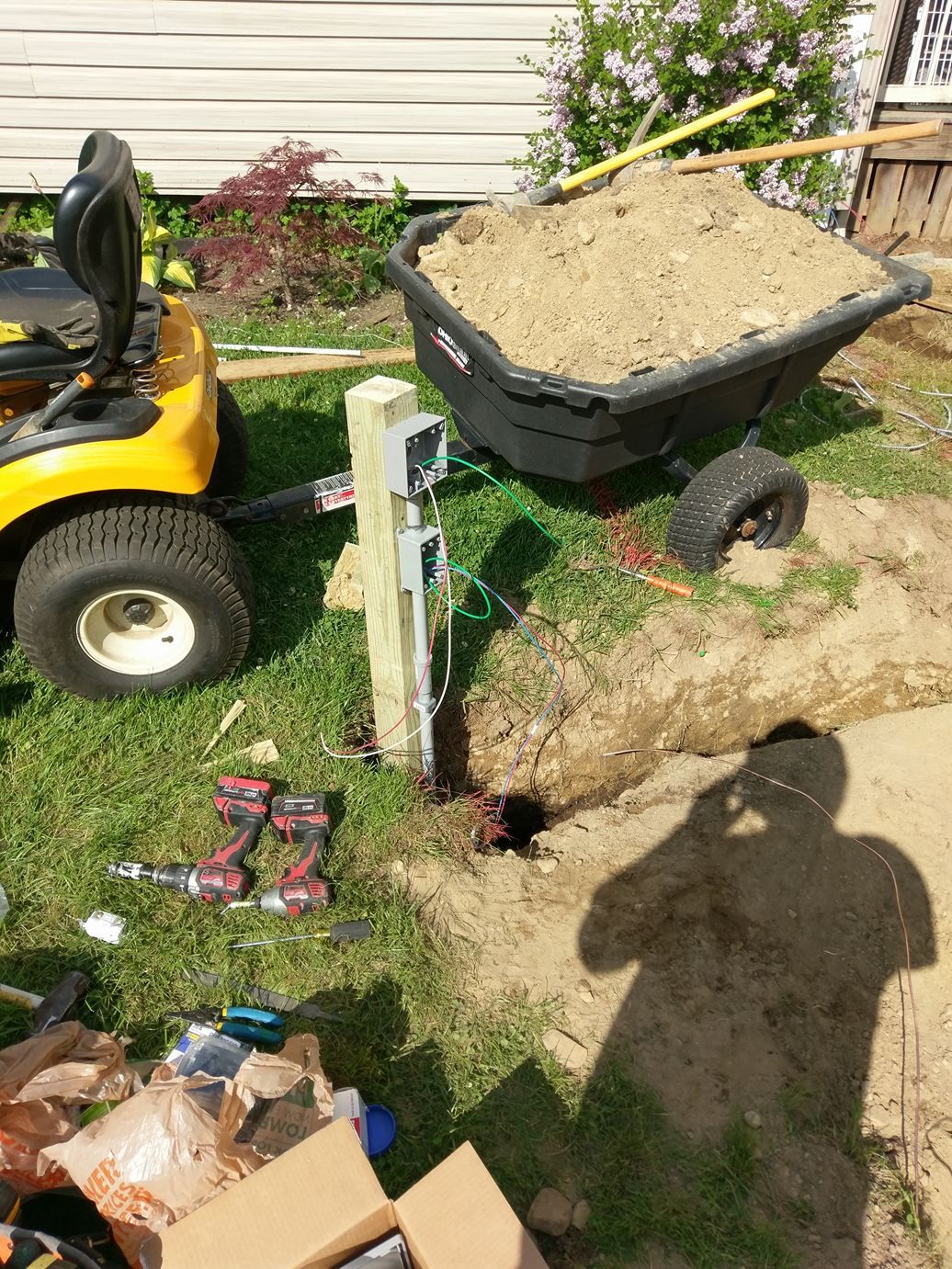 A yellow lawn mower is sitting next to a wheelbarrow filled with dirt.