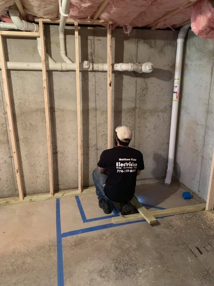 A man is kneeling down in a basement looking at pipes.