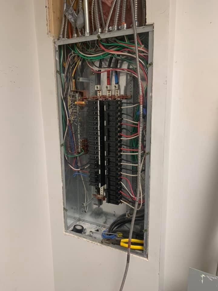 A electrical box with a lot of wires coming out of it is hanging on a wall.