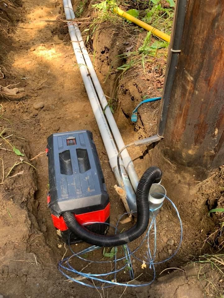 A vacuum cleaner is sitting in the dirt next to a pipe.