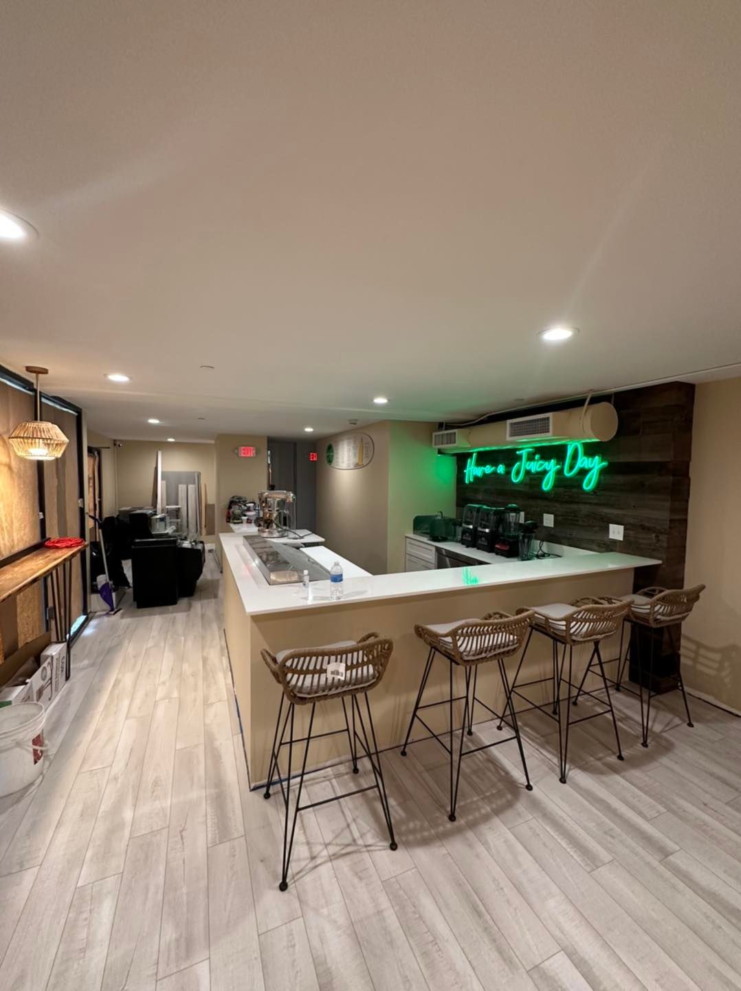 A kitchen with a bar and stools and a neon sign on the wall.