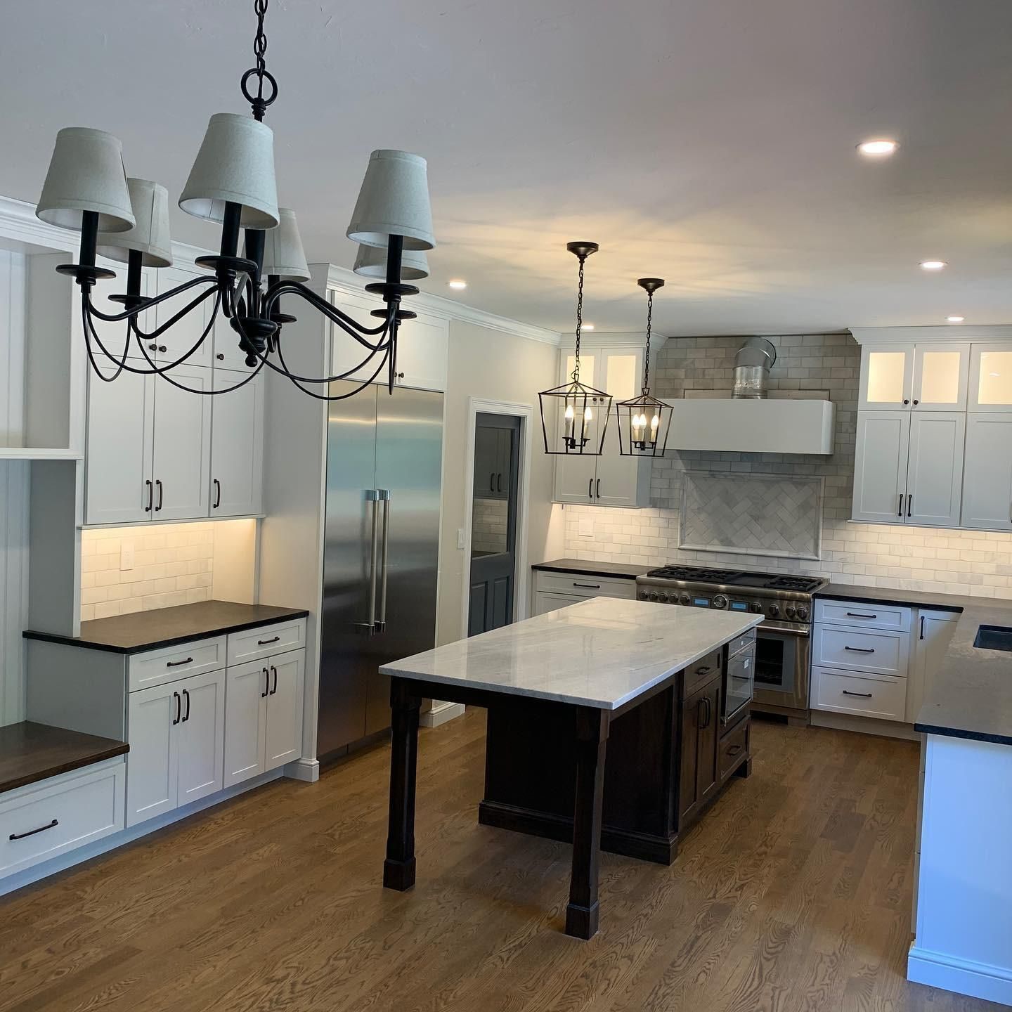 A kitchen with white cabinets, stainless steel appliances, a large island, and a chandelier.