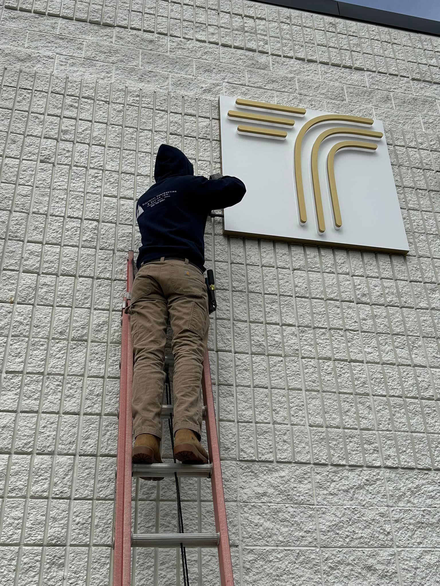 A man is climbing a ladder to install a sign on the side of a building.