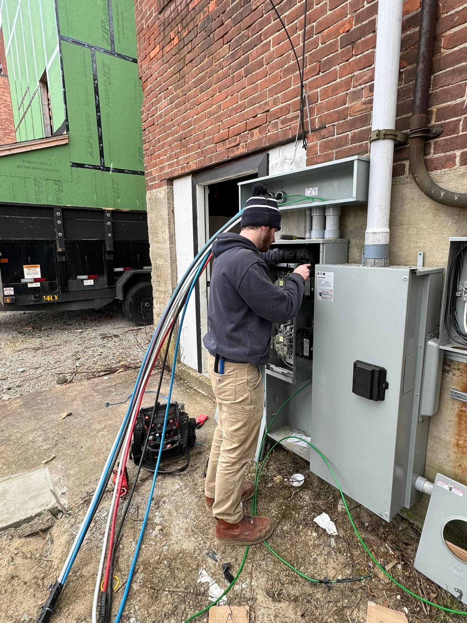 A man is working on an electrical box outside of a building.