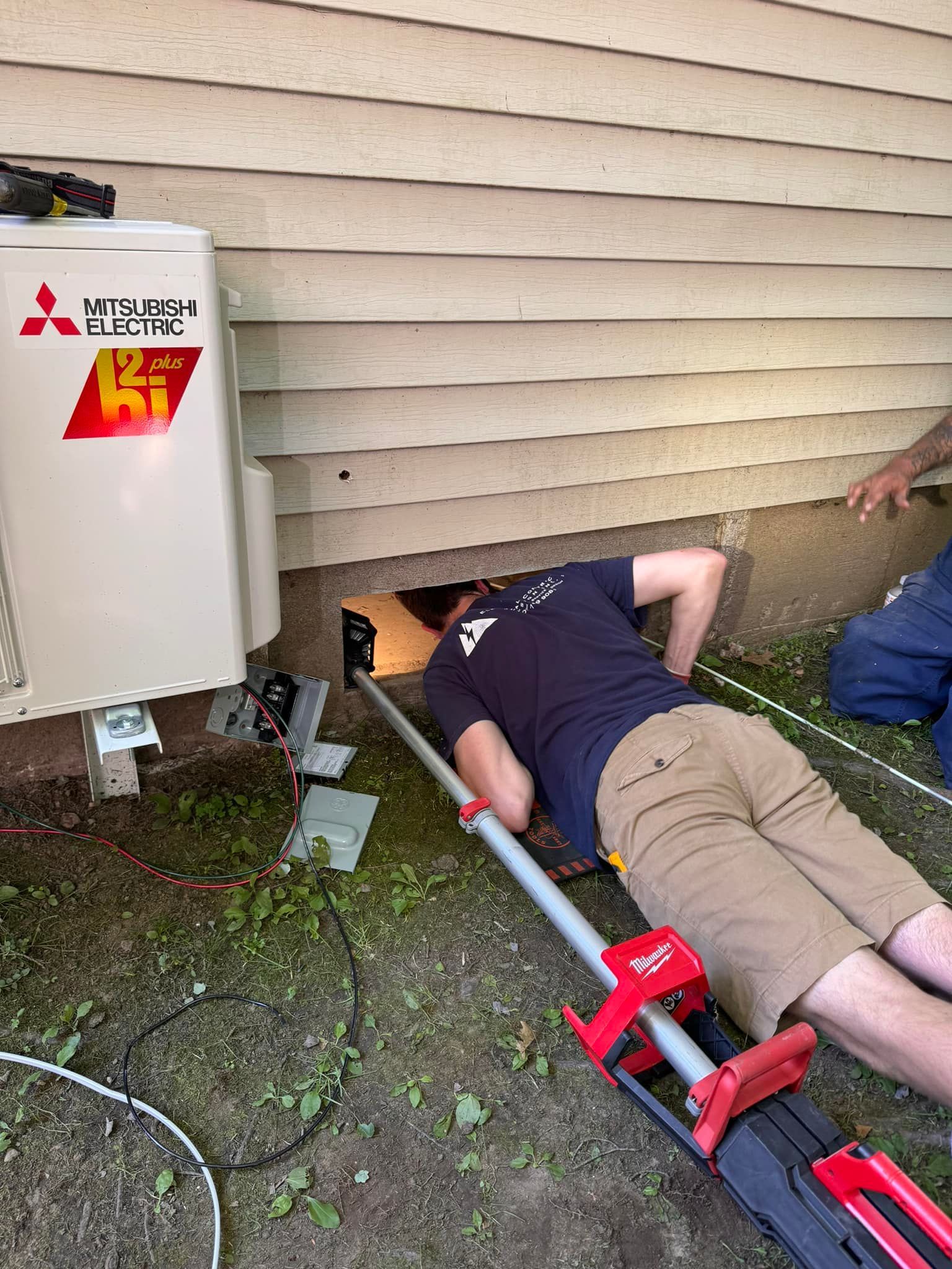 A man is laying on the ground next to a mitsubishi air conditioner.