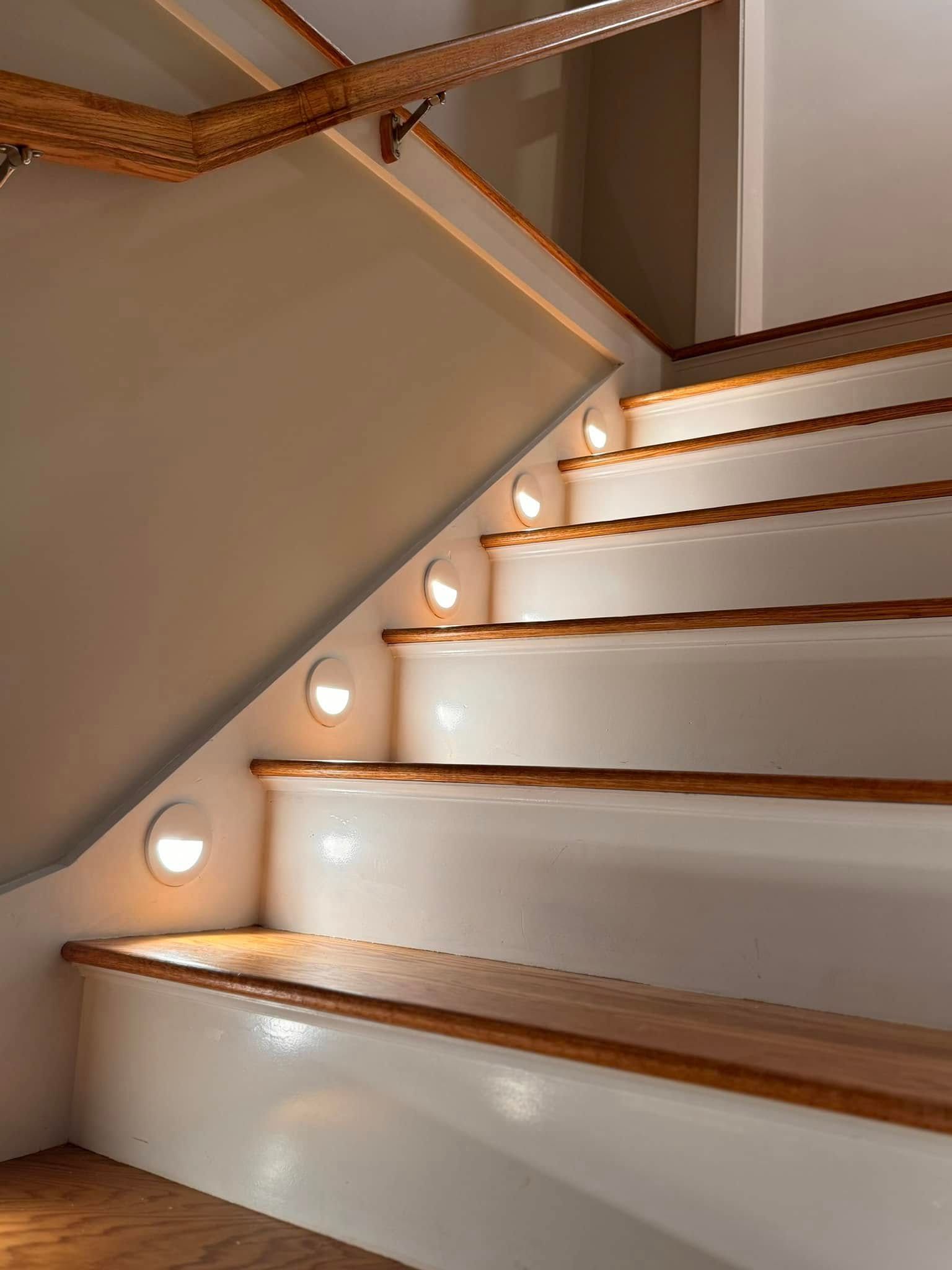 A white staircase with wooden steps and lights on the steps.